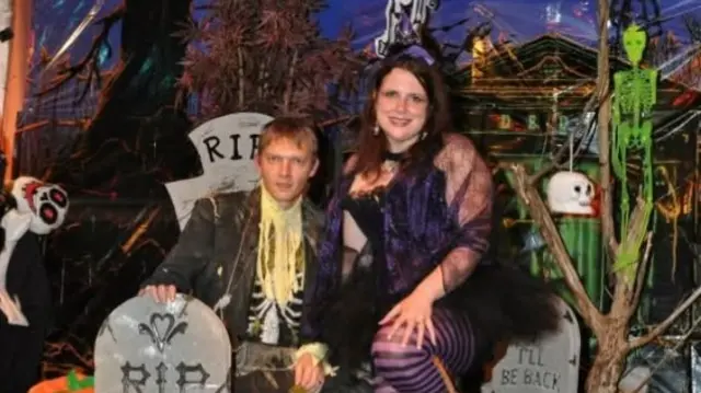 Kevin Hobbins dressed as a zombie next to his wife, dressed at a witch surrounded by fake gravestones and skeletons