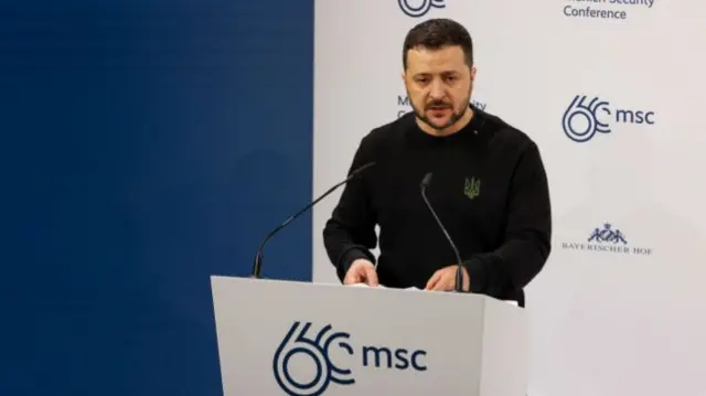 President Zelensky stood behind a lectern in black long-sleeved shirt bearing the Ukrainian trident in military green over the left side of his chest