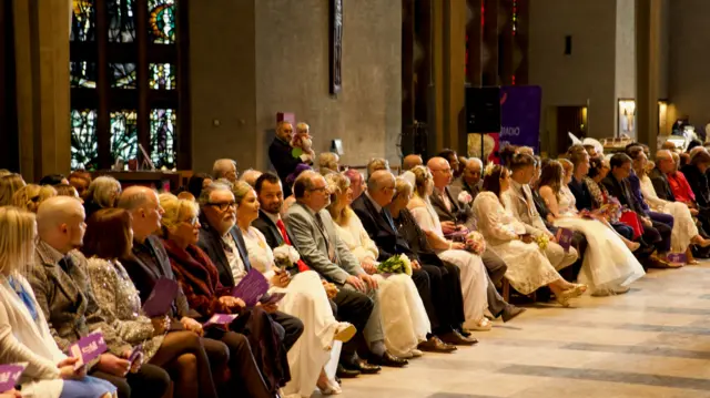 Couples sat next to each otehr in a row in the cathedral