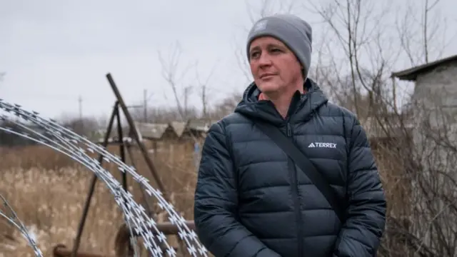 Oleksandr, wearing a hat and a dark jacket, stands next to barbed wire