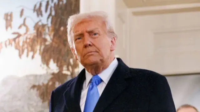 Donald Trump walking through the White House in black coat, white shirt and baby blue tie