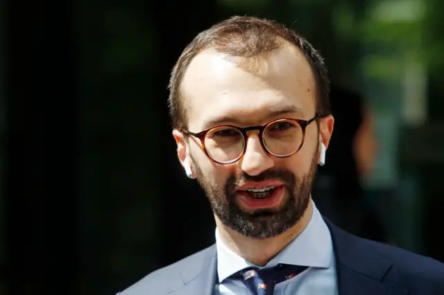 Serhiy Leshchenko wearing tortoise shell glasses, ear pods and a navy suit as he stands outdoor