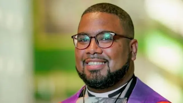 Reverend Nitano Muller dressed in purple and red shawl, wearing glasses