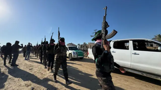 Armed gunman line a road and walk beside white vehicles