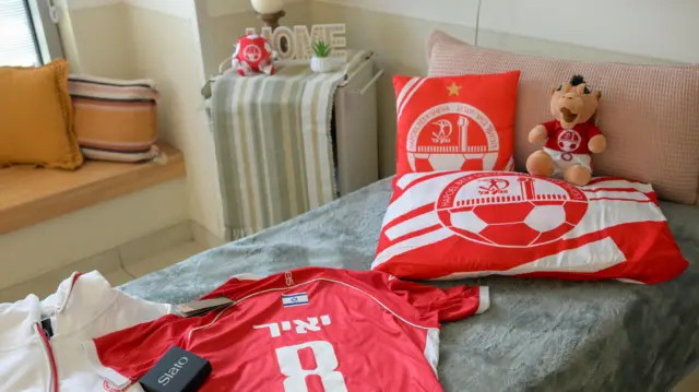 A hospital room decorated with a red football shirt and other club merchandise, with a sign saying "home" on the bedside table