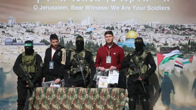 Two of the hostages stand on stage with three armed men