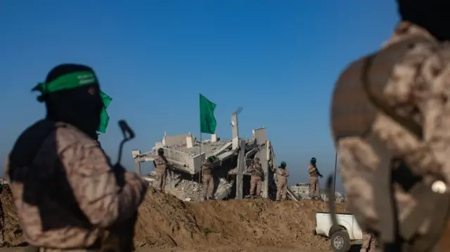 Fighters from Hamas's armed wing stand in front of a destroyed building in Gaza