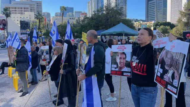 People standing in Hostage Square in Tel Aviv holding signs showing pictures of the hostages still held in Hamas