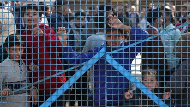 Children stand behind a blue fence, waiting for the Palestinian prisoners to arrive