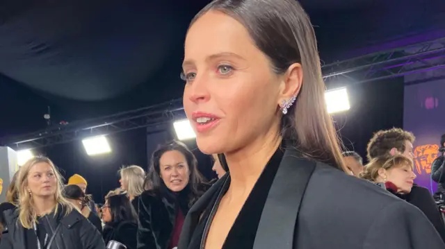 Felicity Jones wears black dress and blazer on Bafta red carpet.