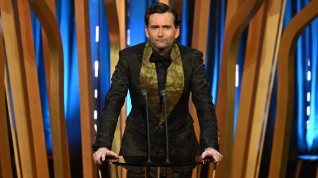 Actor David Tennant in front of a lectern on the Bafta stage. He is wearing a black suit with gold lapels