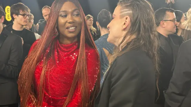 Ashionye Ogene wears a red sequinned dress next to someone wearing a black blazer.