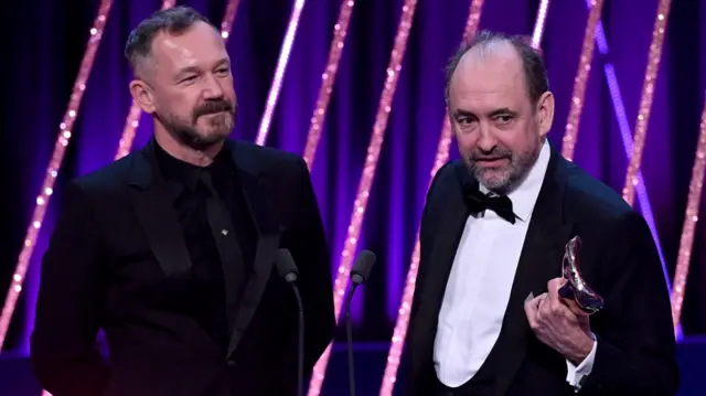 Lee Sandales and Nathan Crowley accept the Production Design Award for 'Wicked' on stage during the EE BAFTA Film Awards 2025 at The Royal Festival Hall on February 16, 2025 in London, England