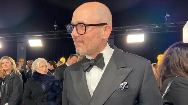 Edward Berger wears a black tux, glasses and bow tie on the red carpet.