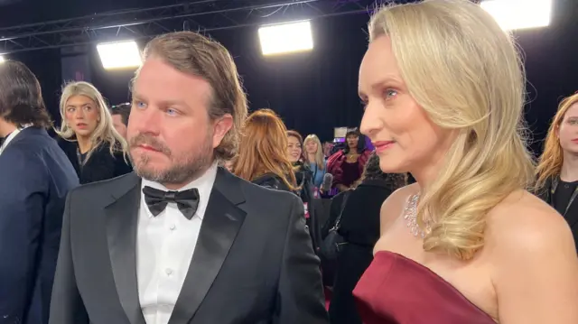 Brady Corbet wears a black suit alongside a woman on the red carpet.