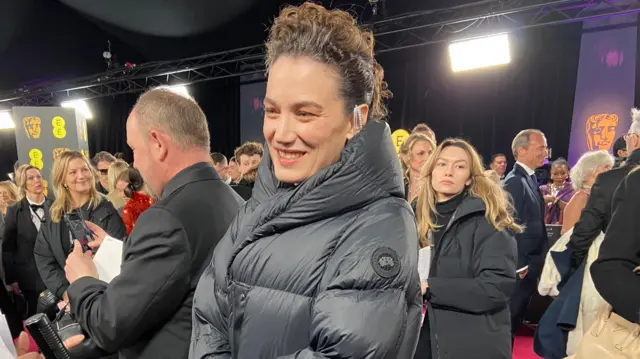 Coralie Fargeat wears a black puffer jacket on the red carpet.