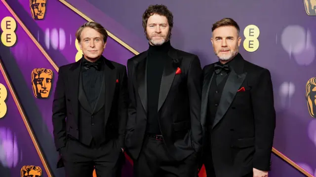 Mark Owen, Howard Donald and Gary Barlow wearing matching black suits with red handkerchiefs in their breast pockets.