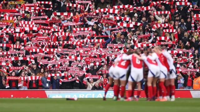 A general view of Arsenal fans holding up scarves in support as the players of Arsenal huddle prior to kick-off