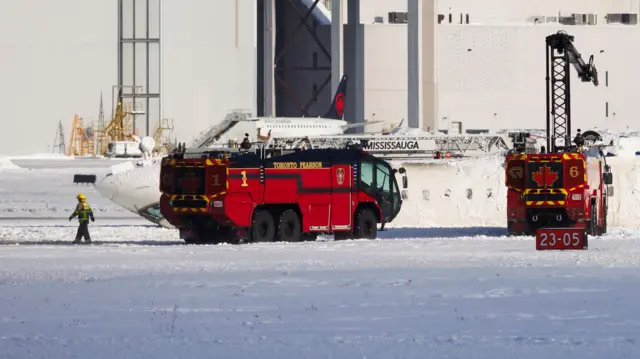 Fire trucks beside a plane flipped upside down on a snowy runway.