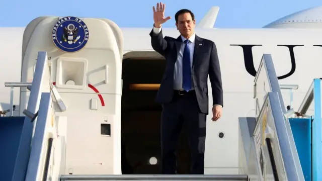 U.S. Secretary of State Marco Rubio waves in front of an airplane which has a 'secretary of state' logo on its door