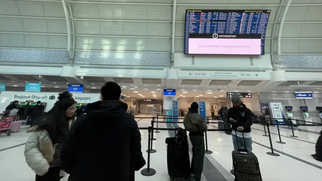 Several people at the Toronto Pearson International Airport’s Terminal 3. There is a big departure board above.