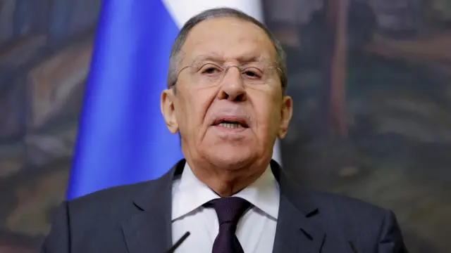 Sergei Lavrov speaking. He wears a dark grey suit, plum-coloured tie, and glasses