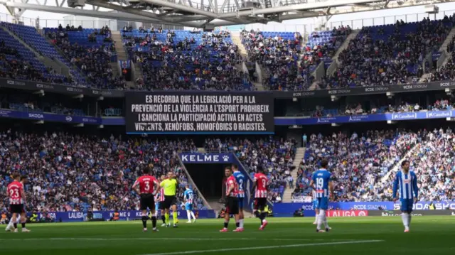 Match referee Guillermo Cuadra Fernandez signals he is stopping play due to crowd behaviour as an anti-racism, homphobia and xenophobia message is displayed on the LED board