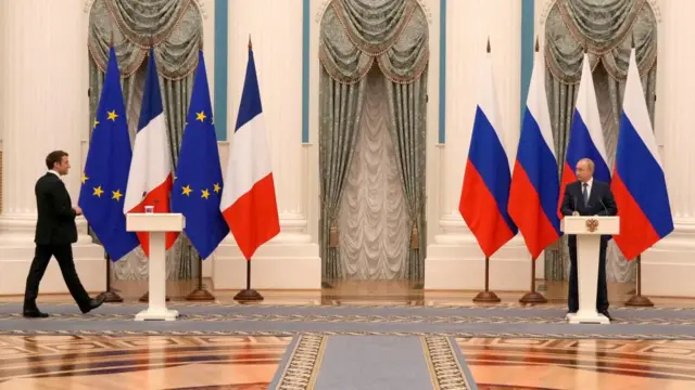 Macron walks towards a lectern - flanked by French and EU flags - while Putin stands behind a separate lectern - flanked by Russian flags - on the opposite side of the room.