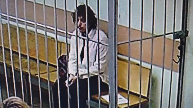 Kalob Byers appears on a screen behind bars in a courthouse