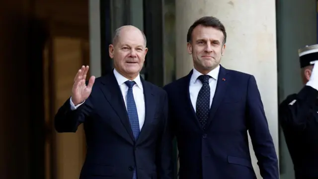 German Chancellor Olaf Scholz waves as he stands next to Macron