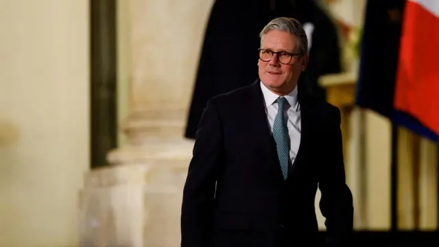 Keir Starmer wears a black suit and green tie outside the Elysee Palace.