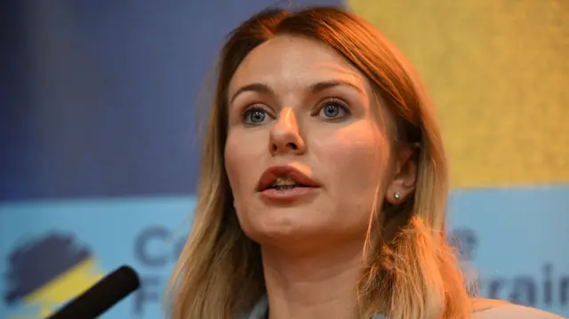 Ukrainian MP Lesia Vasylenko wears a grey blazer and speaks behind a microphone.