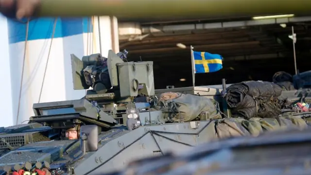 Swedish servicemen with Sweden Armed Force equipment, which includes a Swedish flag, sit inside a tank