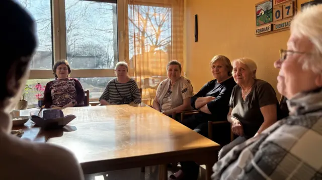 A group of people sit around a table in Oberhausen. The room has yellow walls and a big table in the middle.