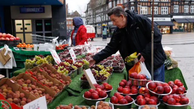 A man picks up a punnet grapes at a fruit and vegetable stall on a high street.