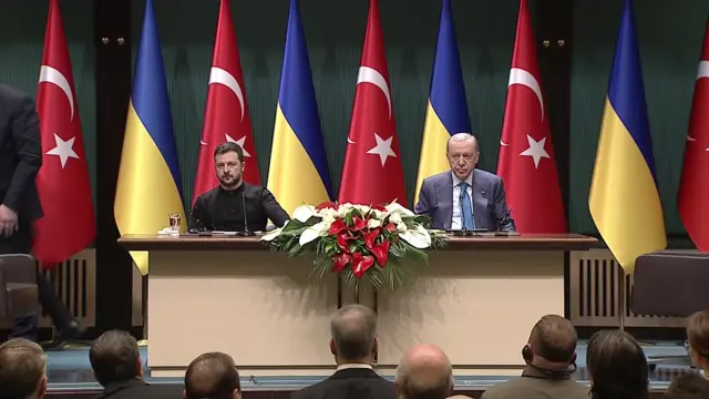 On a long table, with the flags of Ukraine and Turkey behind them, sits Zelensky and Erdogan. They both look serious as the look ahead of them to a crowd of reporters sat down