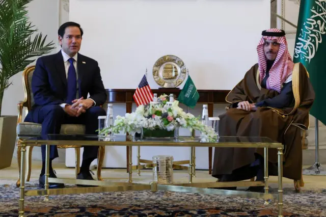 Marco Rubio (left) and Prince Faisal bin Farhan Al Saud sit at a table adorned with flowers and the flags of their respective countries