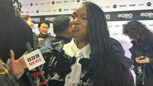 Nao speaks to the BBC on the red carpet at the Mobo awards. She has long black hair and brown eyes.