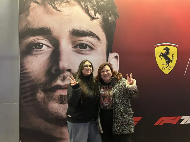 Jessica and Alice pose in front of a picture of Charles Leclerc