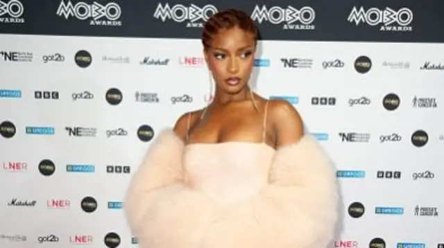 Singer Ayra Starr in a strappy pale pink gown with a fur piece and long earrings.