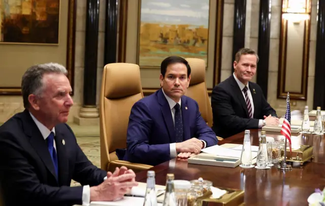 Marco Rubio (centre) sits at a large wooden table with a US flag. He's flanked by his National Security Adviser Mike Waltz and US Middle East envoy Steve Witkoff