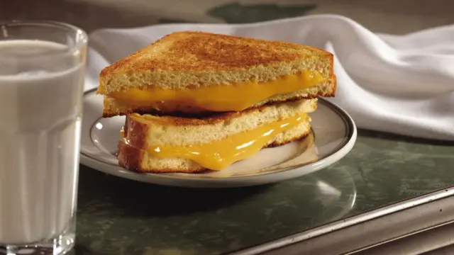 A stock photo of cheese oozing out of a toastie, with milk in a glass beside