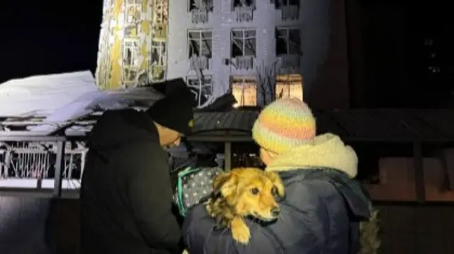 People stand with their dog outside a damaged building in Ukraine's southern city of Odesa, following a Russian attack