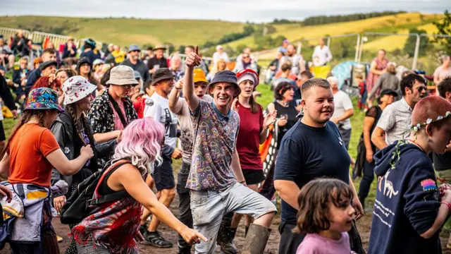 A large group of mixed-age people, walking through a muddy field whilst wearing bucket hats.