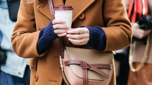 A woman holding a white takeaway coffee cup