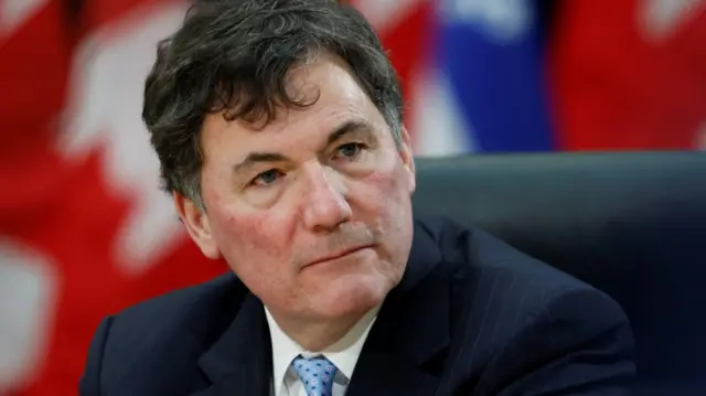 Canada's Finance Minister Dominic LeBlanc in a striped black suit in front of a Canadian flag
