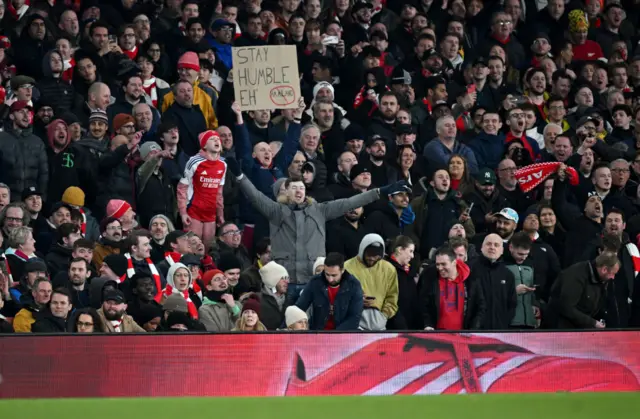A fan of Arsenal holds up a sign which reads "Stay Humble EH"