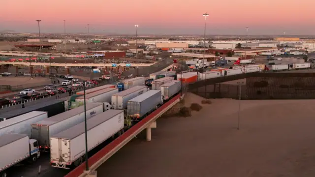 A queue of trucks form on the motorway with cars stuck in traffic in the background.