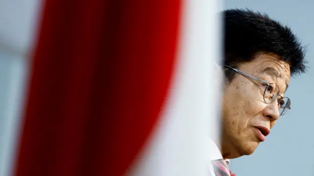 Japan's Finance Minister Katsunobu Kato wears glasses near a flag of Japan