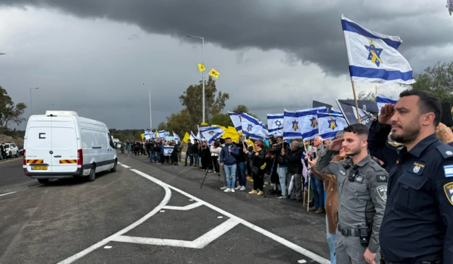 Police and citizens salute and wave flags as a convoy of vans carrying coffins drives past